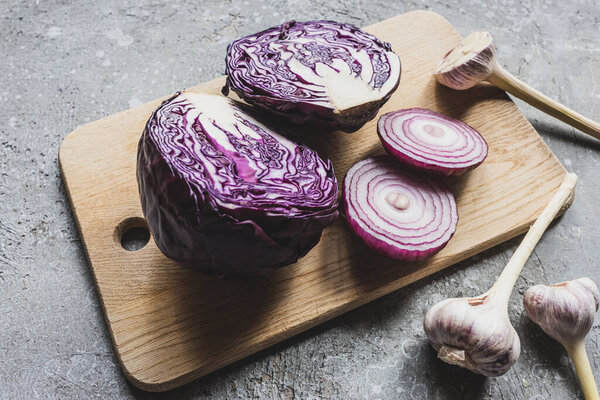 red cabbage, onion and garlic on wooden cutting board on grey concrete surface