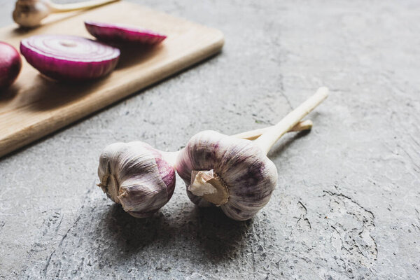 selective focus of garlic near onion on wooden cutting board on grey concrete surface