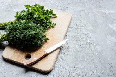 green parsley and dill on cutting board with knife on grey concrete surface clipart