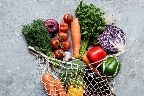 вид сверху на свежие спелые овощи в струнном мешке на серой бетонной поверхности
