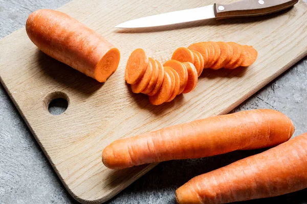 fresh ripe carrot slices on wooden cutting board with knife on concrete surface