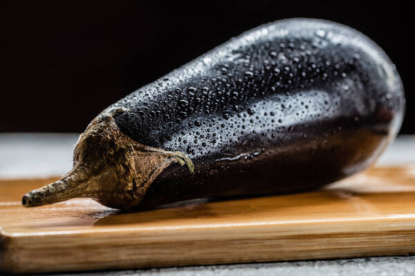 fresh ripe eggplant with water drops on wooden board isolated on black