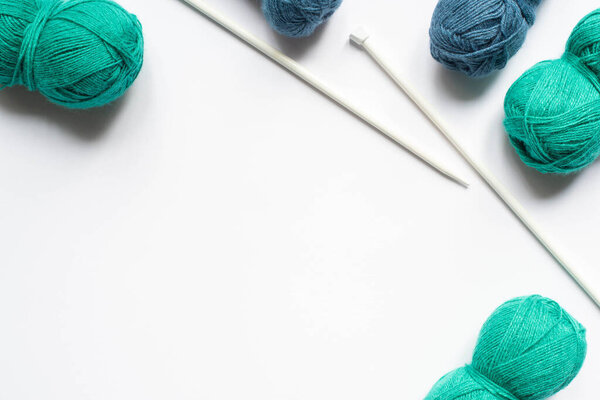 top view of blue and green wool yarn and knitting needles on white background