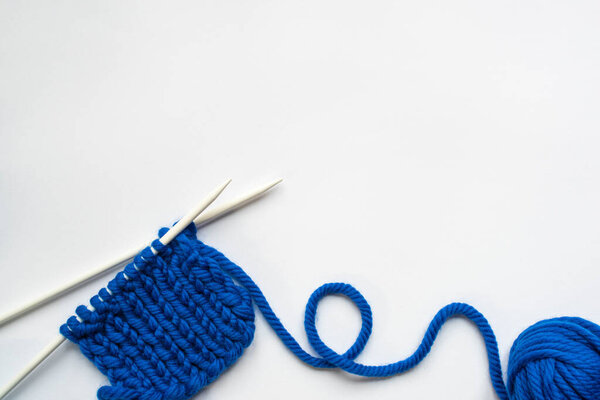 top view of blue wool yarn and knitting needles on white background