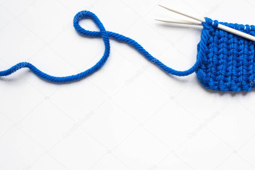 top view of blue wool yarn and knitting needles on white background
