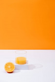 fresh orange juice in glass near cut fruit on white surface isolated on orange