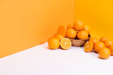 fresh ripe oranges in bowl on white surface on orange background clipart
