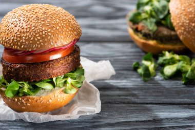selective focus of tasty vegan burgers with microgreens and vegetables served on wooden table clipart