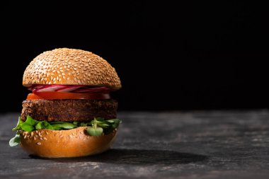 tasty vegan burger with microgreens, radish and tomato served on textured surface isolated on black clipart