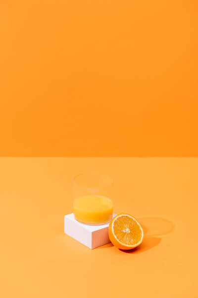 fresh orange juice in glass near half of orange and white cube isolated on orange