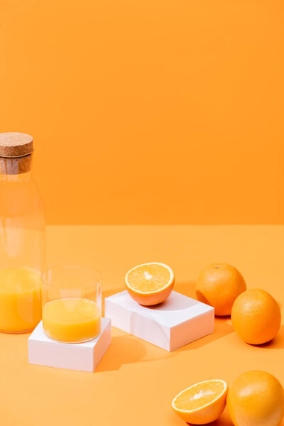 fresh orange juice in glass and bottle near ripe oranges and white cubes isolated on orange