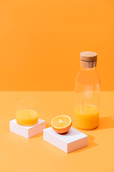 fresh orange juice in glass and bottle near cut orange and white cubes isolated on orange