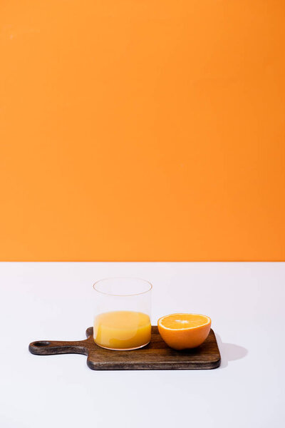 fresh orange juice in glass near cut fruit on wooden cutting board on white surface isolated on orange