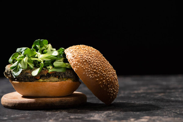 tasty vegan burger with microgreens served on wooden board isolated on black