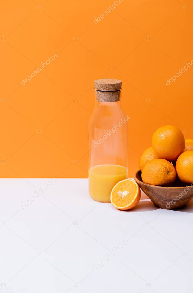 fresh orange juice in glass bottle near oranges in bowl on white surface isolated on orange