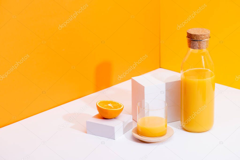 fresh orange juice in glass and bottle near ripe orange on white surface on orange background