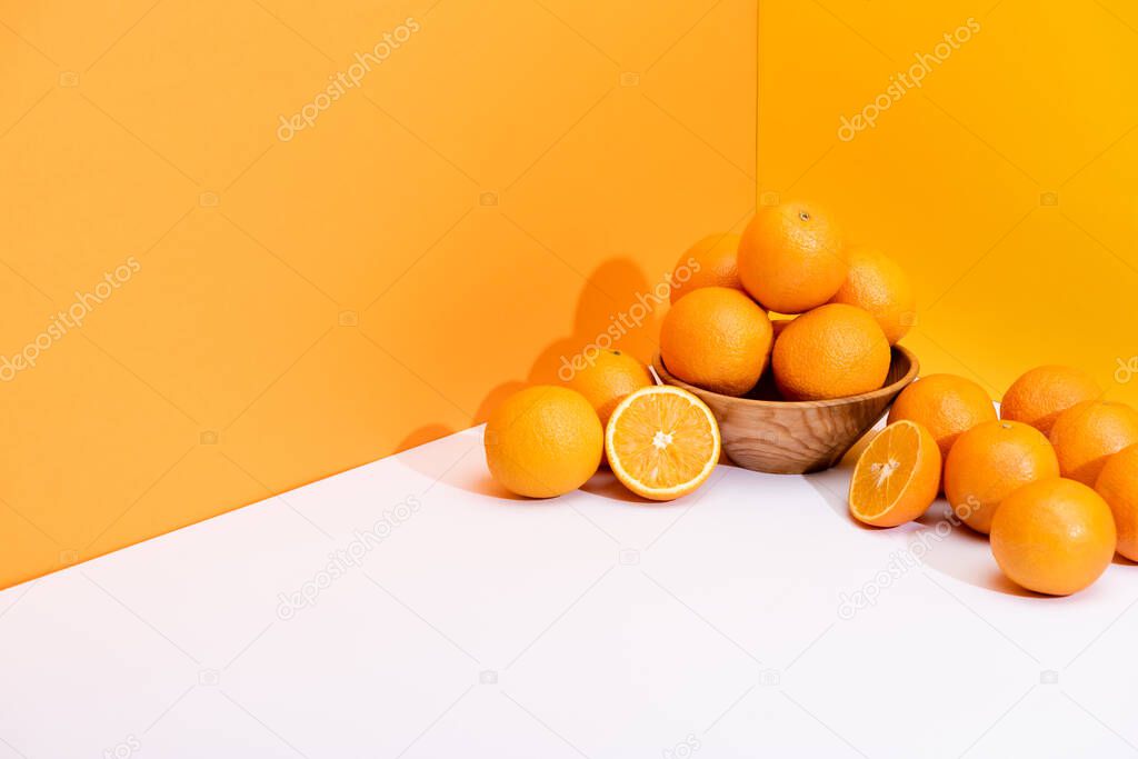 fresh ripe oranges in bowl on white surface on orange background