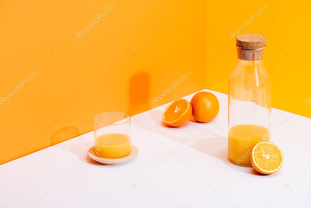 fresh orange juice in glass and bottle near ripe oranges on white surface on orange background