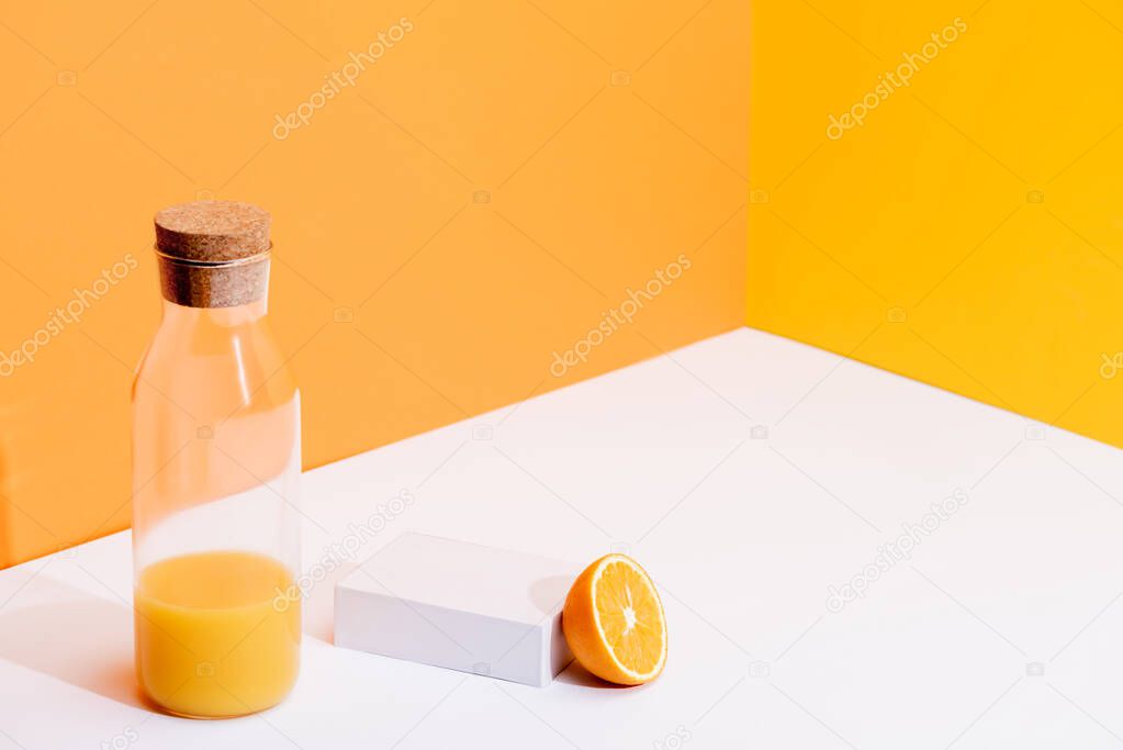 fresh orange juice in glass bottle near ripe orange on white surface on orange background