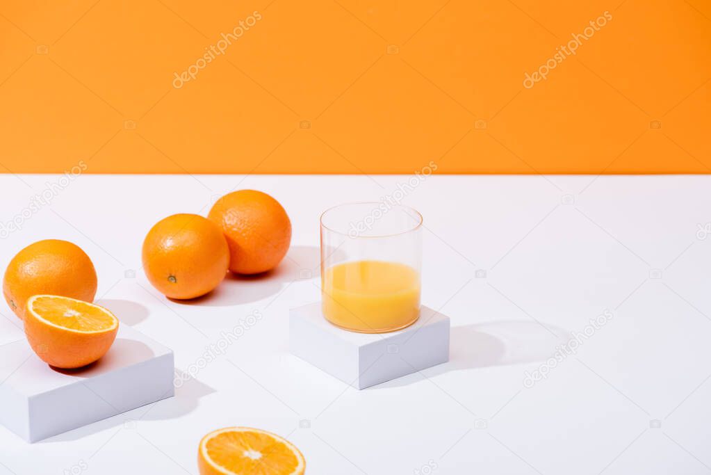 fresh orange juice in glass near ripe oranges on white surface isolated on orange