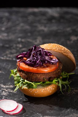 Domatesli, kırmızı lahana ve turplu dokuma üzerine servis edilen yeşillikli vegan burger.