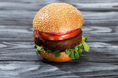 tasty vegan burger with vegetables served on wooden table clipart