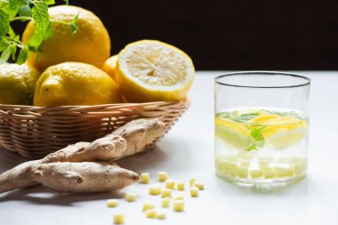 Limon sepetinin yanında naneli limonata ve siyah arka planda zencefil kökü.