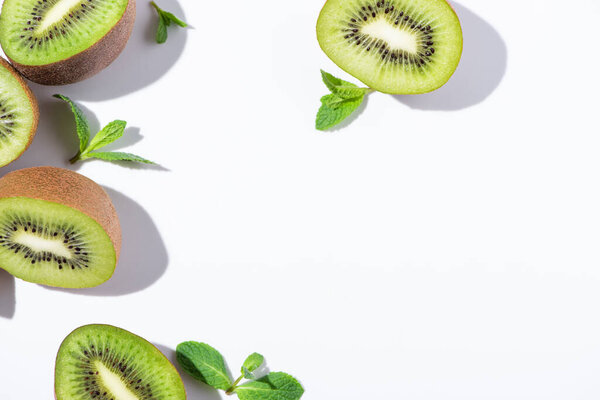 top view of ripe and green kiwi fruit halves near peppermint on white 