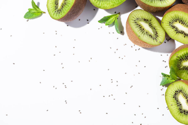 top view of organic kiwi fruit halves near peppermint and black seeds on white 