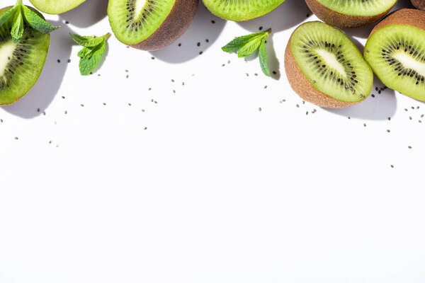 верхний вид органических фруктов киви половинки около зеленой мяты и черные семена на белом
 