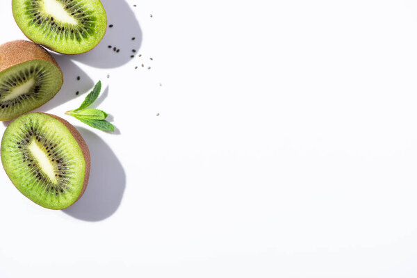 top view of kiwi fruit halves near green peppermint and black seeds on white 