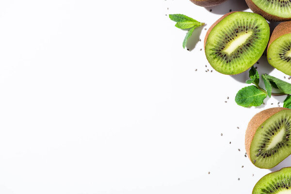 top view of tasty kiwi fruit halves near green peppermint and black seeds on white 
