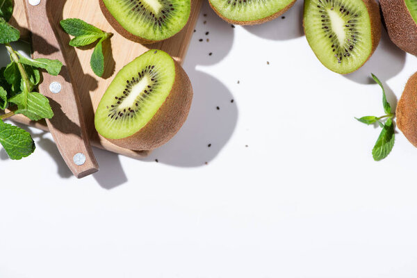 top view of tasty kiwi fruit halves near green peppermint on cutting board on white 