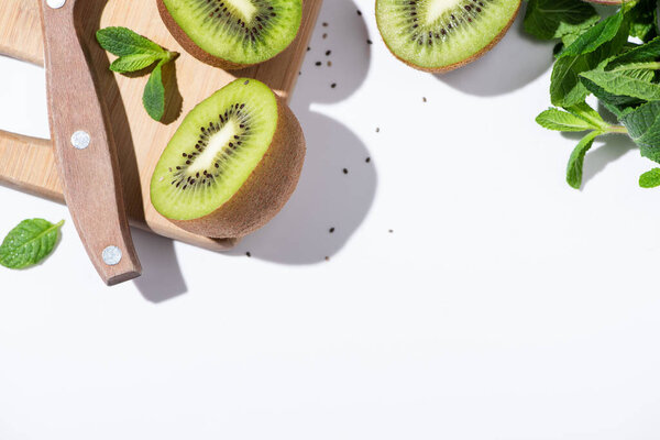 top view of fresh kiwi fruit near green peppermint on cutting board on white 