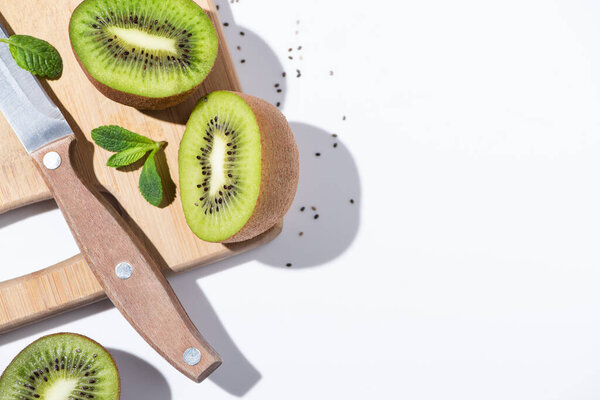 top view of fresh kiwi fruits near peppermint on cutting board on white 