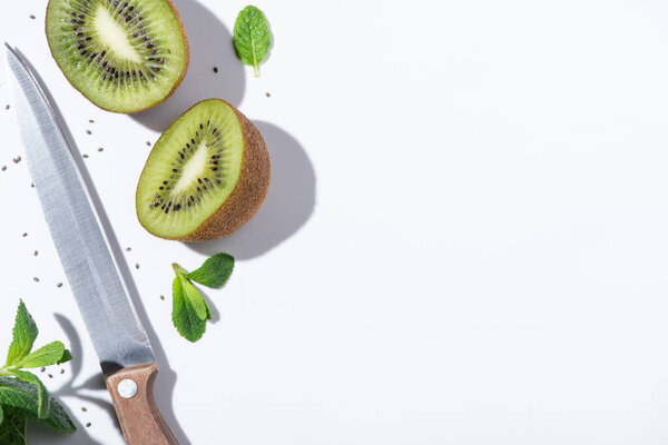 top view of tasty kiwi fruits near green peppermint, knife and black seeds on white 