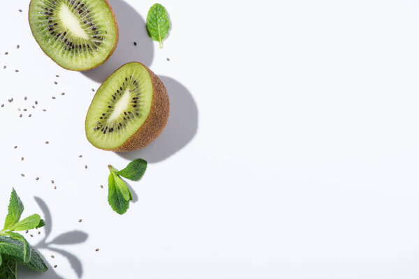top view of ripe kiwi fruits near fresh peppermint and black seeds on white 