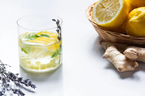 白を基調にレモンと生姜の根のバスケットの近くにミントとラベンダーの枝を持つガラスの新鮮な生姜レモネード — ストック写真