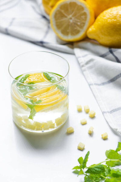 selective focus of fresh ginger lemonade in glass near napkin and lemons on white background