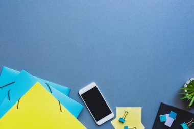 Kağıt dizinlerinin yanında boş ekranı ve mavi arkaplanda kırtasiyesi olan akıllı telefonun üst görünümü