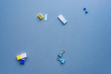 Top view of pencil sharpener, binder clips and erasers on blue background clipart