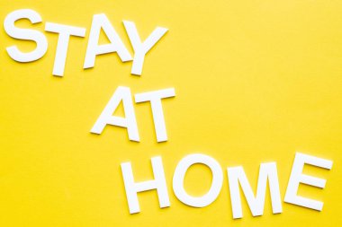 Top view of lettering stay at home on yellow surface clipart