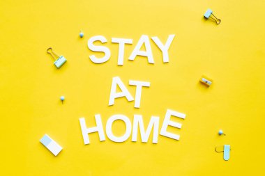 Top view of stay at home lettering near binder clips and pencil sharpener on yellow surface clipart