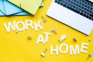 Top view of work at home lettering near laptop and stationery on yellow background clipart