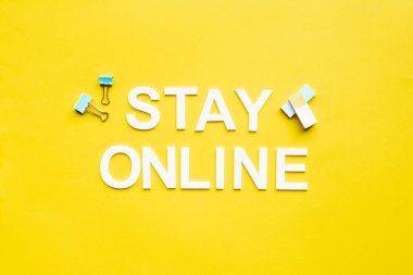 Top view of stay online lettering near binder clips and erasers on yellow surface clipart