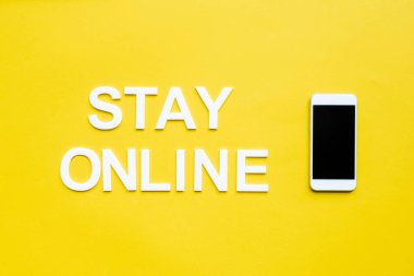 Top view of stay online lettering and smartphone with blank screen on yellow background clipart