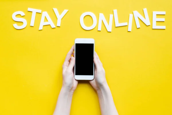 白い画面と文字でスマートフォンを保持している女性のトリミングビューは 黄色の表面にオンラインで滞在 — ストック写真