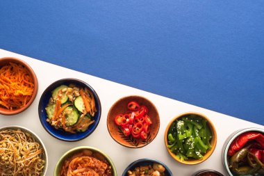 top view of bowls with korean traditional side dishes on blue and white  clipart