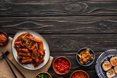 Kore topokkisi kimbap, yemek çubukları, garnitür tabakları ve tahta yüzey üzerindeki pamuk peçetenin yanında. 