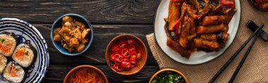 Kimbap, kimchi, yemek çubukları, garnitür tabakları ve tahta yüzey üzerindeki pamuk peçetenin yanında Kore topokkisi. 